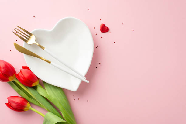 istock Ideal 8 March dinner idea, top-view photo of romantic table layout, heart-shaped platter, elegant utensils, sequins, heart motifs, and tulip bouquet on blush pink background, with blank area for text 2030179197