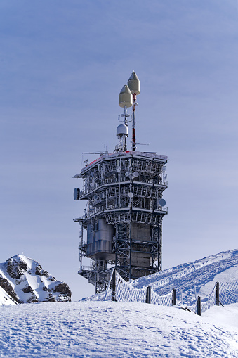 Concrete and metal communications tower on top of Titlis mountain on a sunny winter day with mountain panorama. Photo taken February 21st, 2024, Titlis, Engelberg, Switzerland.