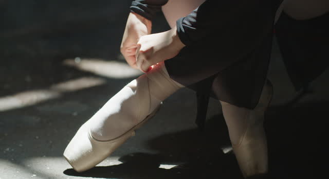 Close-up, Unrecognizable Ballerina Ties Ballet Shoes Preparing for Performance.