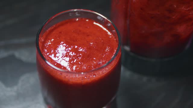 Red berry smoothie in a glass. Close up. Black wooden table.