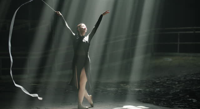 Silhouette of Ballerina performing with white ribbon in dramatic light at dark hall.