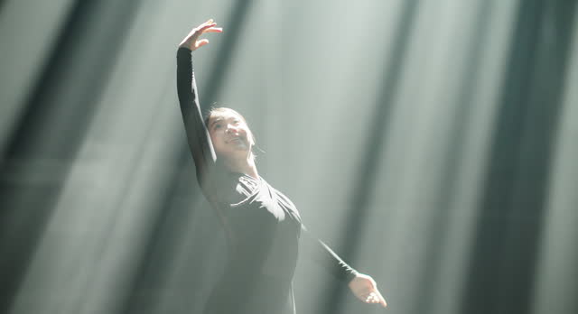 Silhouette of Ballerina performing hands flow movements in spotlights.