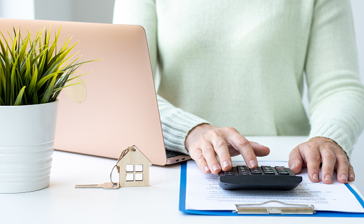 Woman calculating mortgage cost on calculator. Expenses on refinancing of home loan. Real estate investment concept