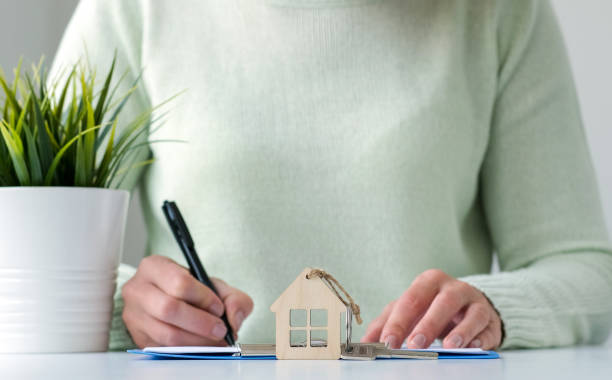 mujer firmando un préstamo hipotecario o un acuerdo de seguro con un llavero en forma de casa en primer plano - real estate mortgage document key contract fotografías e imágenes de stock