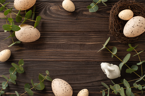 Sophisticated green Easter design. Top-view photo featuring eggs, a small nest, a ceramic bunny, and eucalyptus sprigs arranged on a wooden base, with blank space for text or promotions