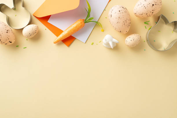 istock Easter crafting joy concept. Overhead shot of envelope with card, pastel eggs, ceramic bunny, baking molds, vibrant sprinkles, and fresh carrot set on a beige surface with space for text or ads 2030247712