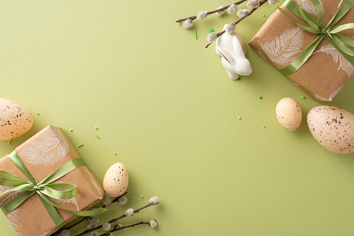 Provincial Easter design concept. Top view of earth-toned gift wrappings, petite rabbit sculpture, quail eggs featuring natural designs, pussy willow on green hue background with space for messages