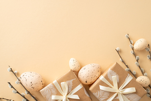 Serene Easter composition proposal. Top view angle capturing nature-inspired gift wrapping, quail eggs, pussy willow boughs, on a minimalist beige backdrop with empty space for inscriptions