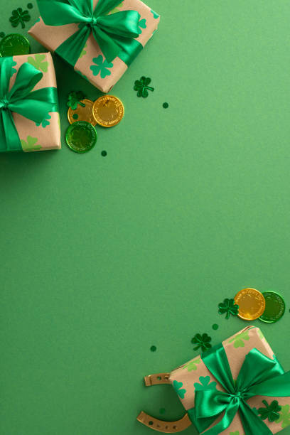 istock St. Patrick's thematic vertical overhead concept with shamrocks, lucky coins, gift containers, a horseshoe, and confetti spread on a green area, leaving space for text 2030247747