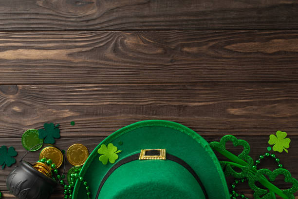 istock Spellbinding St. Patrick's scenario from top view, filled with shamrocks, leprechaun headwear, currency coins, treasures, party lenses, garlands, positioned on wooden tableau, space for text or promos 2030247755
