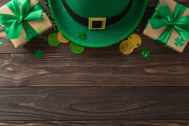 istock Charming St. Patrick's theme layout from top view, displaying green clovers, fairy hat, lucky coins, wrapped gifts, garlands, confetti, organized on wooden setting, with space for messaging or adverts 2030247757