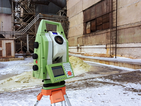 Total station at work on a blurred industrial background. Electronic total station - modern geodetic instrument combines engineering tacheometer and a 3D laser scanner.