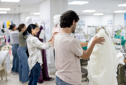 Rear view of a group of fashion design students sewing dresses on a mannequin at an atelier
