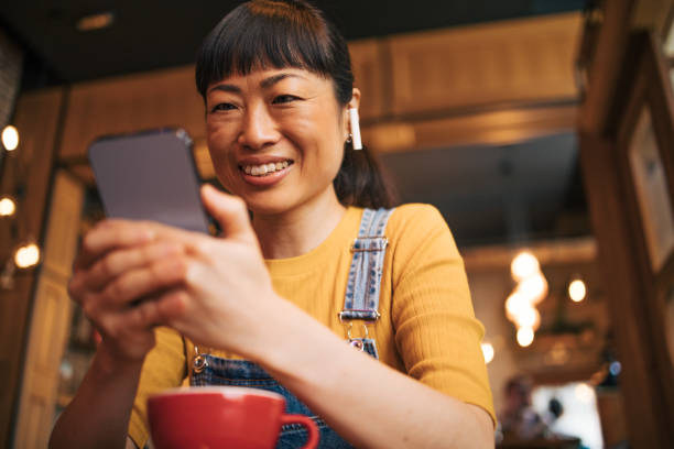 istock Yapanese woman using mobile phone and enjoying coffee at cafe 2030273134