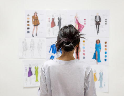 Rear view of a Latin American fashion design student looking at sketch illustrations at the atelier