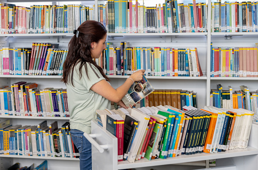 Latin American librarian organizing books in bookshelves at the library - education concepts