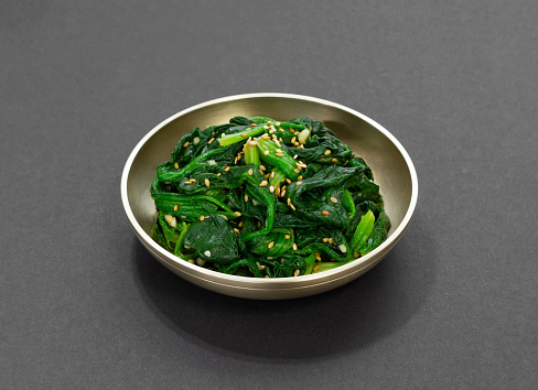 Spinach Salad. A traditional Korean side dish of spinach moochim served in a brass bowl. Boild spinach seasoned with sesame oil.