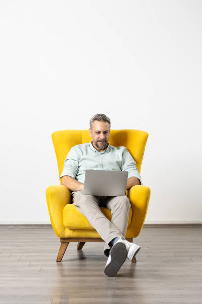 istock Handsome man sitting in armchair and using laptop. White studio background. 2030299951