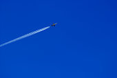 a passenger plane with vapour trails high in the blue sky