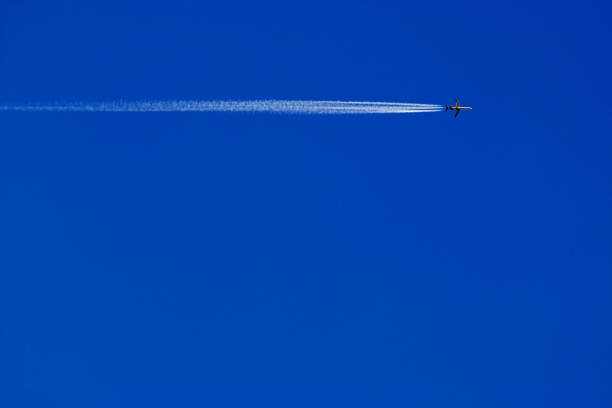 a passenger plane with vapour trails high in the blue sky