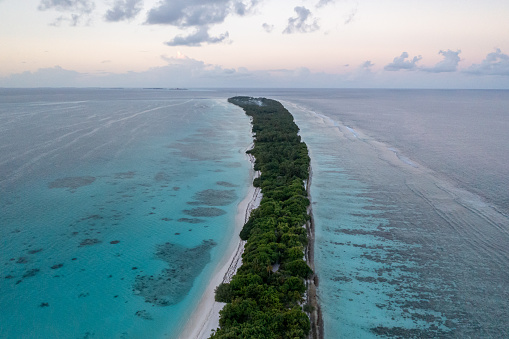 Narrow Island Dhigurah on Maldives in turquoise blue water in the evening. Coral Reefs are seen through the water.