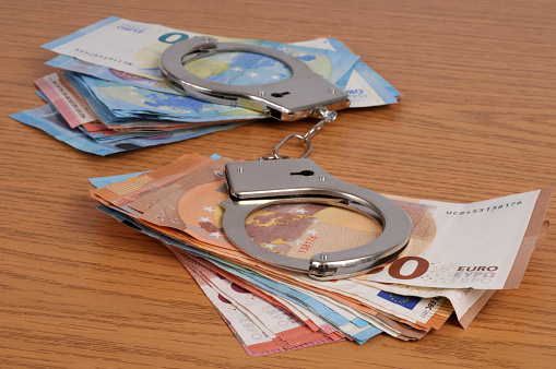 Financial crime concept with handcuffs on wads of euro banknotes