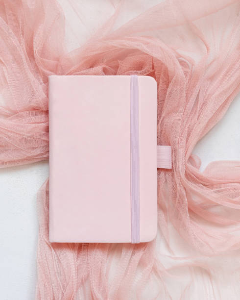istock Pink hardcover notebook on tulle fabric on white table top view, textbook mockup 2030325920