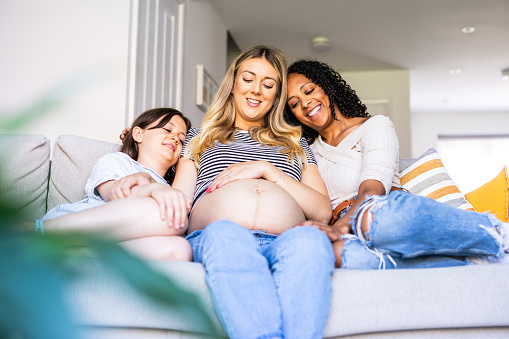 Happy pregnant woman with family relaxing on the sofa - Same sex gay couple expecting a baby and spending quality time together
