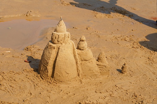 Kids having fun building sandcastles on beach. The boy is carving a sand bridge to his sand castle.\nNikon D810