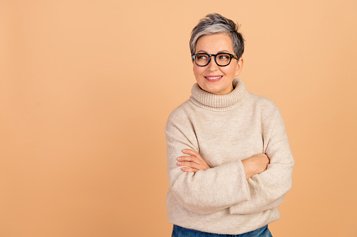 Photo portrait of mature age grandmother wear stylish turtleneck crossed arms looking empty space isolated on beige color background.