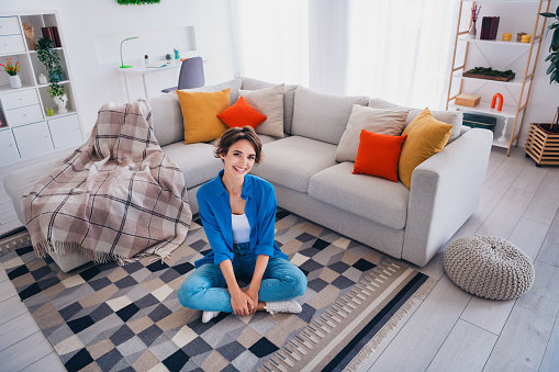 Top view photo of positive good mood girl sitting on floor in new comfortable apartment.