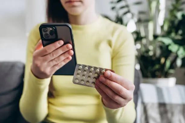 Photo of Selective focus of young lady using smartphone for reading, searching prescription on pills medicine, pill label text about information online, instructions side effects, pharmacy medicament concept