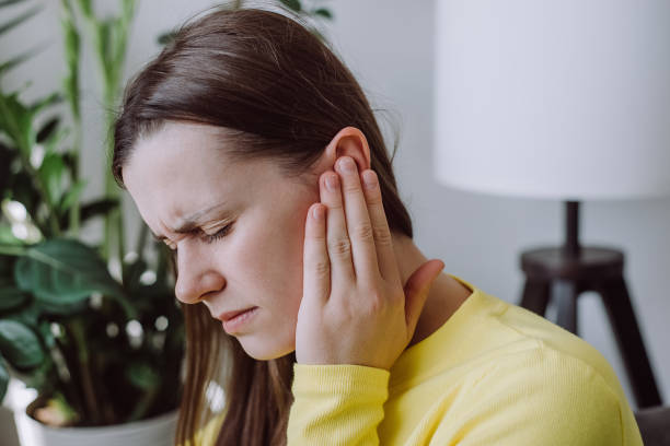 Sick sad young woman has ear pain or earache, hand touch plug ear, suffering painful otitis from loud or noisy sound, inflammation. Health care nerve deaf eardrum disease. Tinnitus concept stock photo