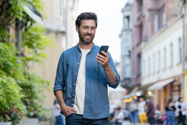 istock Smiling bearded man using smartphone while walking in evening city scene 2030373563