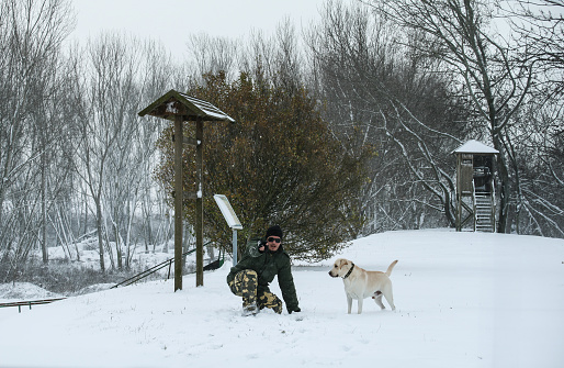 In a serene winter setting, a man and his playful yellow Labrador frolic amidst the snow-covered landscape, embodying the pure joy of companionship and outdoor adventure.