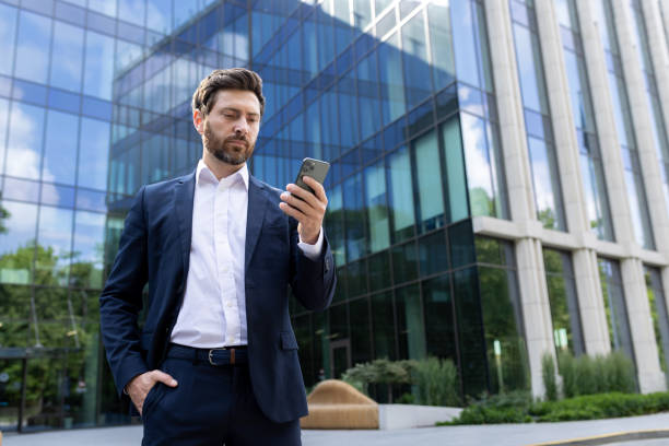 istock Confident businessman with beard using smartphone outside modern office building 2030390120