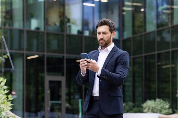 istock Confident bearded businessman using smartphone in front of modern office 2030390146