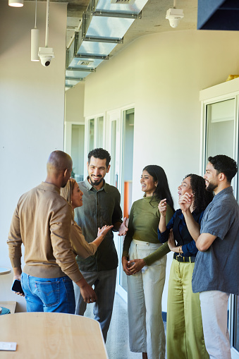 Diverse group of businesspeople talking and laughing while standing together in a corridor of a modern office