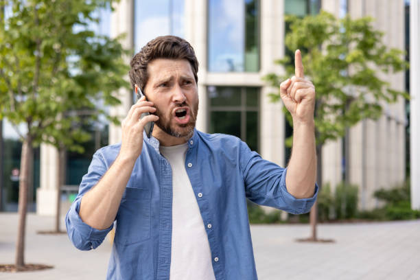 istock Bearded businessman in casual attire gesturing while on phone against office background 2030401077