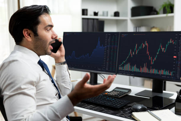 istock Trader calling to consultant or partner with two stock exchange screen. Surmise. 2030402824