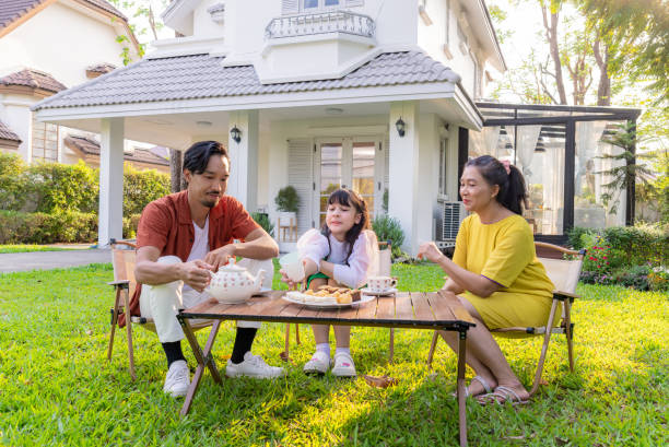Multi-generation Asian family spending their weekend together by having afternoon tea together in green garden outdoor at home on weekend. They are happy and talking, laughing, and spending valuable time together. Holistic Well-Being Home. Diverse age family.
