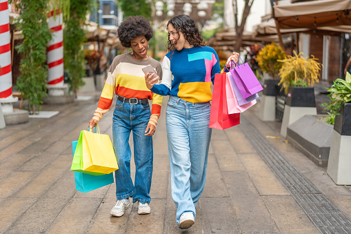 Young women walking with their shopping and looking at a cell phone, carrying bags of different colors.