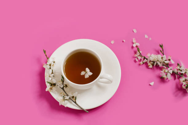 istock White porcelain cup with black tea. Branches of a blossoming apple tree lie on a bright pink background. Spring concept. 2030444515