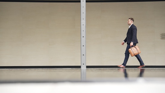 Side view of business people holding suitcase and walking to workplace along the street in urban city. Professional project manager going to meeting while wearing formal suit walk at outdoor. Urbane.