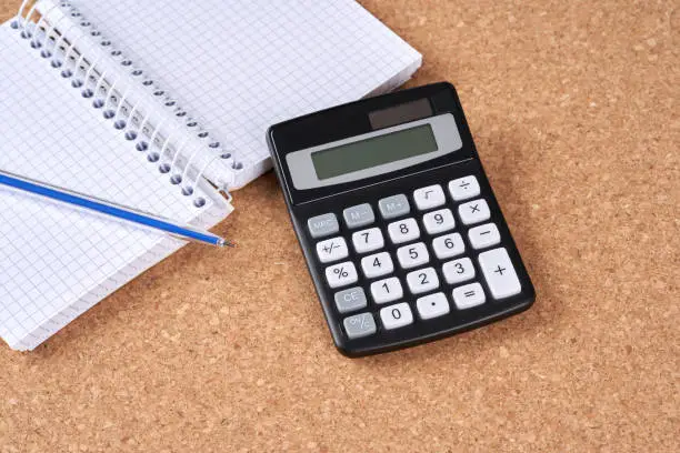 Calculator and pen on a cork plate.