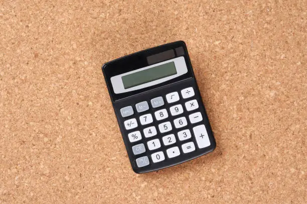 Calculator and pen on a cork plate.