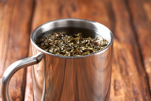 Green tea in a stainless steel mug on an old wooden table.