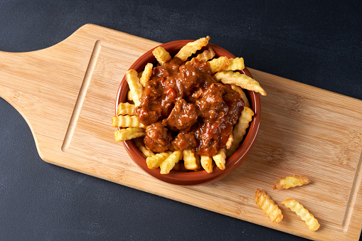 Fried fries with goulash in a red plate.