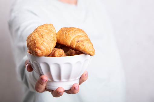 Hands holding a plate with croissants on a blurred background.