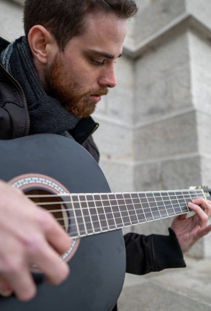 Close-up of a bearded man learning to play the guitar alone in an empty square. Vertical.